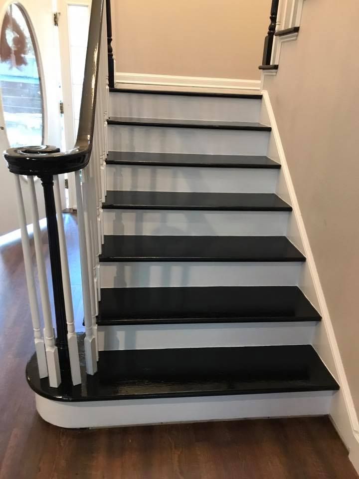 Staircase with black treads and white risers. Dark wooden flooring. Black and white banister. Cream-colored walls.