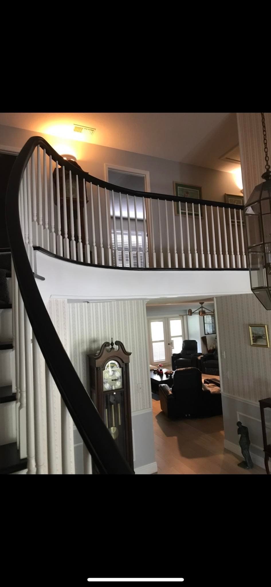 A grand, curved staircase with black banisters and white spindles. A grandfather clock stands below.