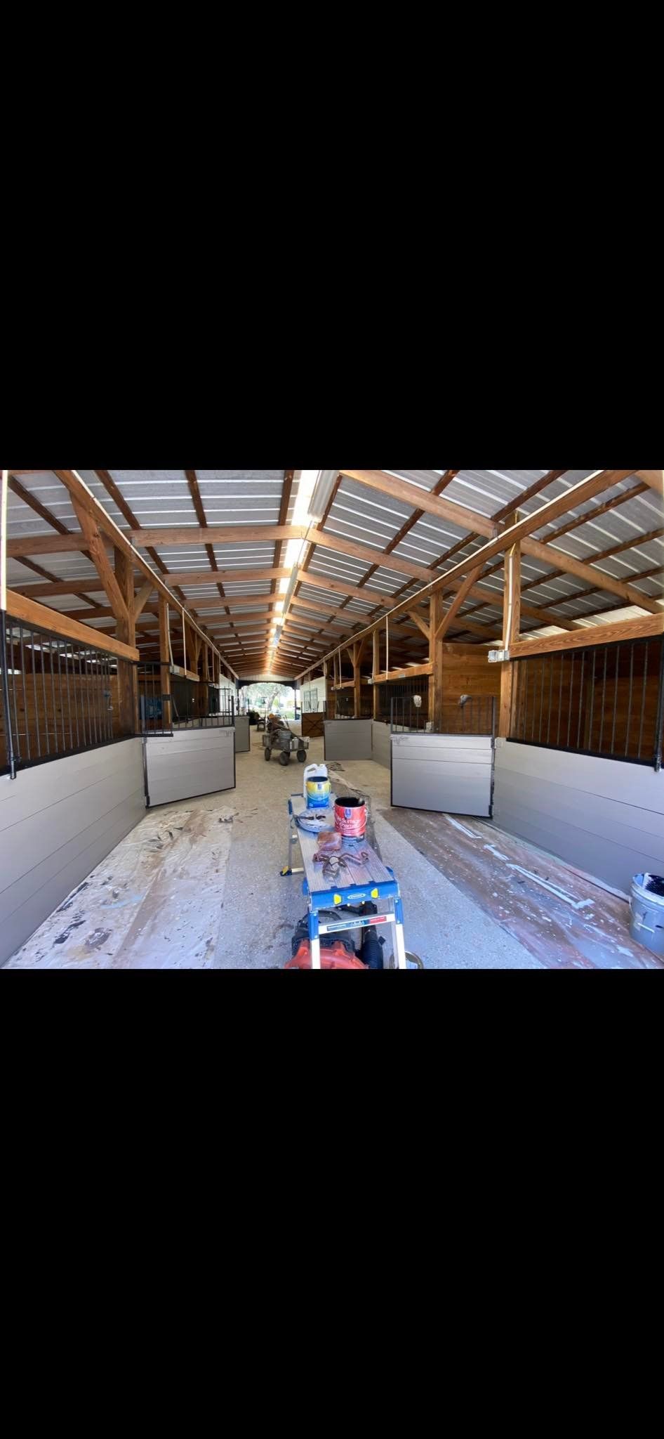 Interior of a barn with wooden beams and a metal roof. A row of stalls is on either side.