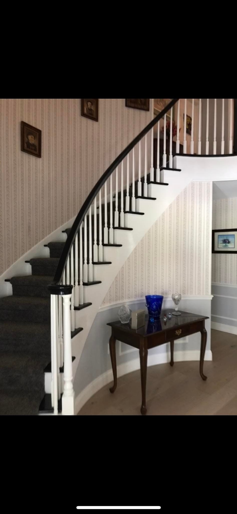A curved staircase with black railing and steps in a light-colored entry hall, with a small table and decor.
