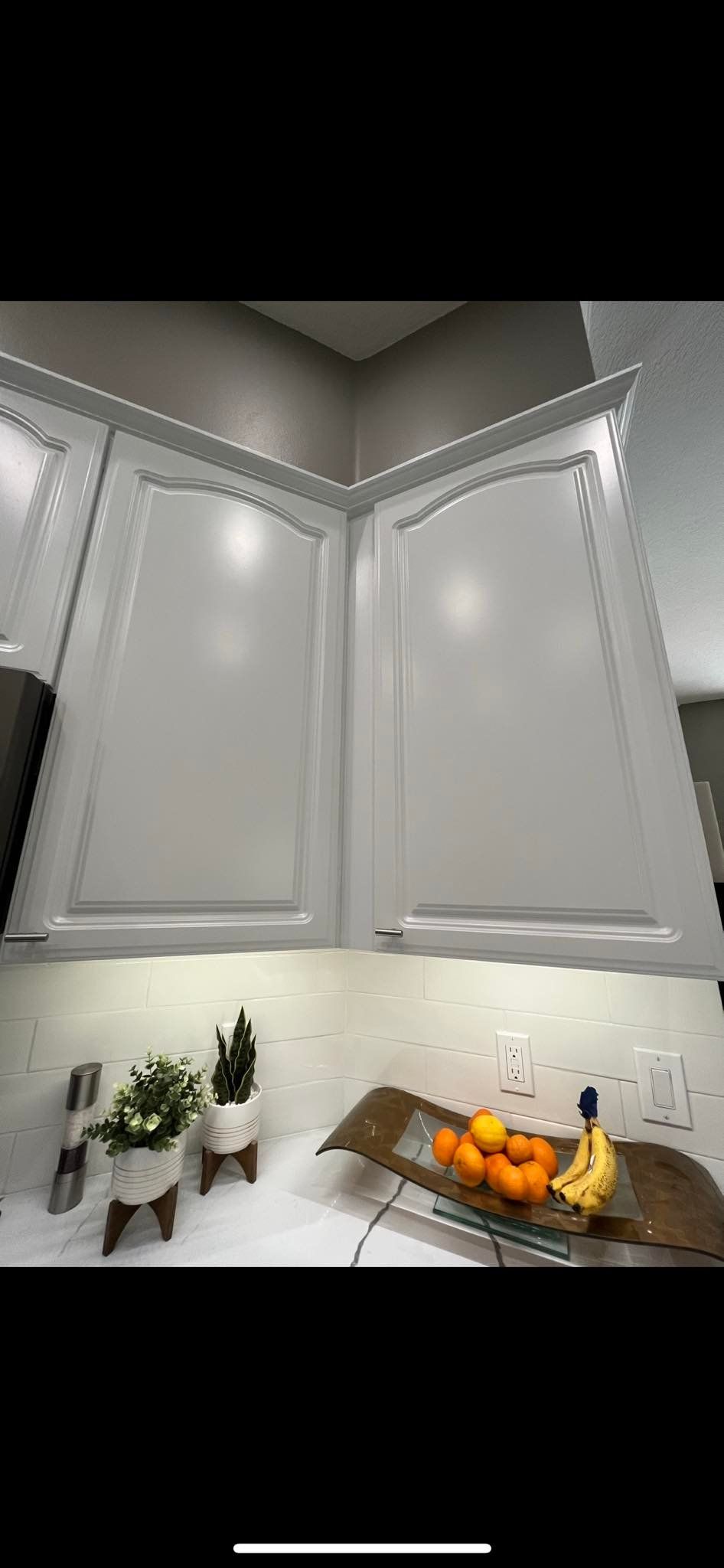 White kitchen cabinets above a countertop with fruit and plants.