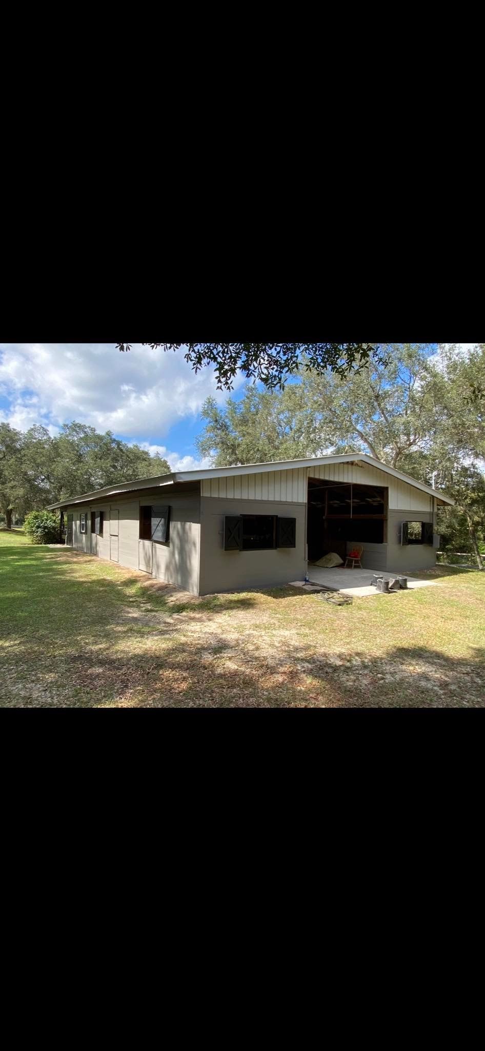 A one-story concrete house with a dark roof surrounded by green grass and trees.