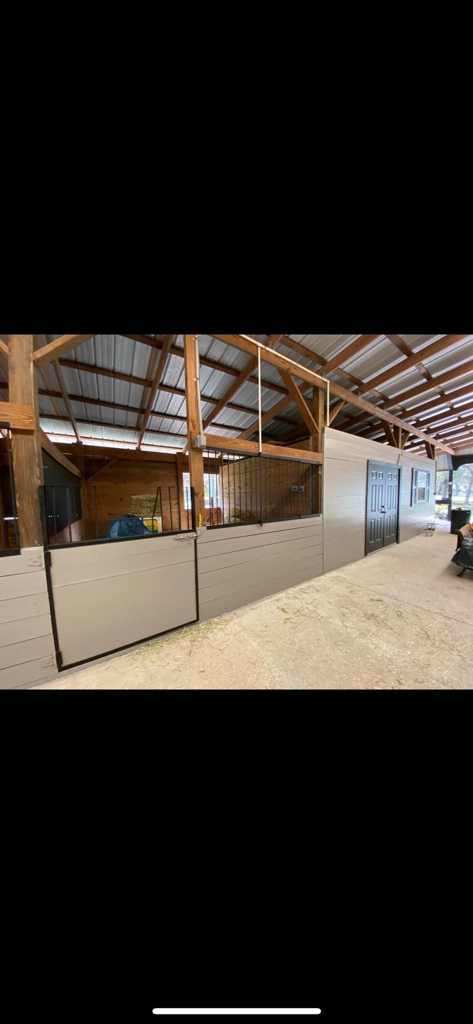 Inside of a barn with light tan walls, and a dirt floor. Roof beams are visible.