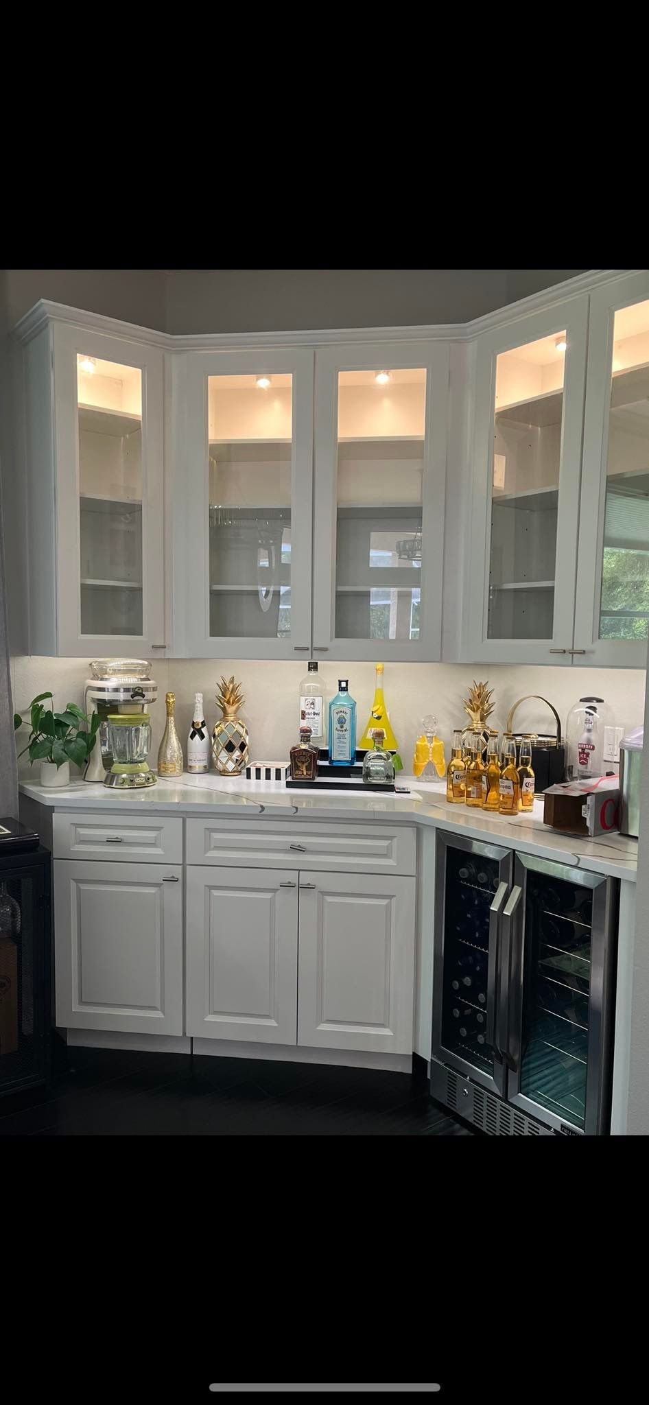 White kitchen cabinets with glass doors, a countertop with bottles, and a wine cooler.
