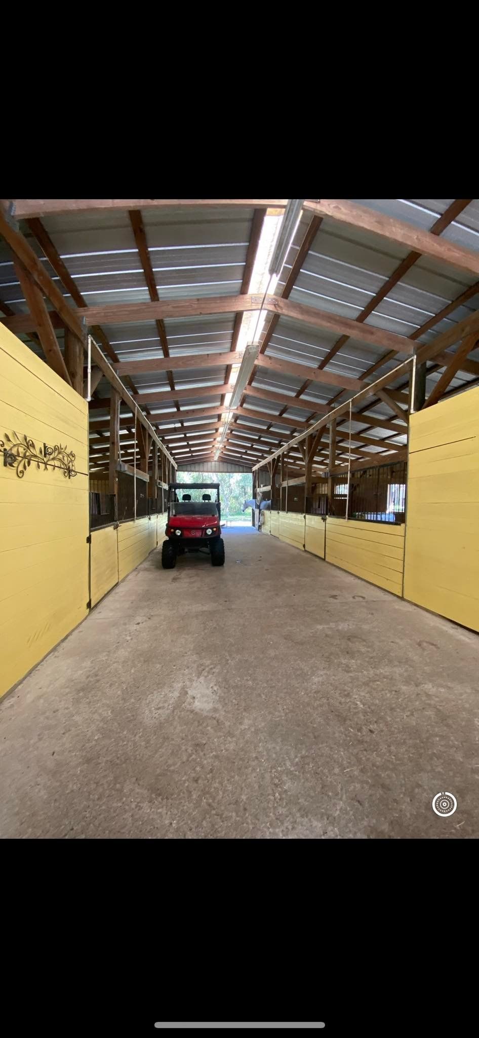A red utility vehicle sits inside a barn with stalls on either side.