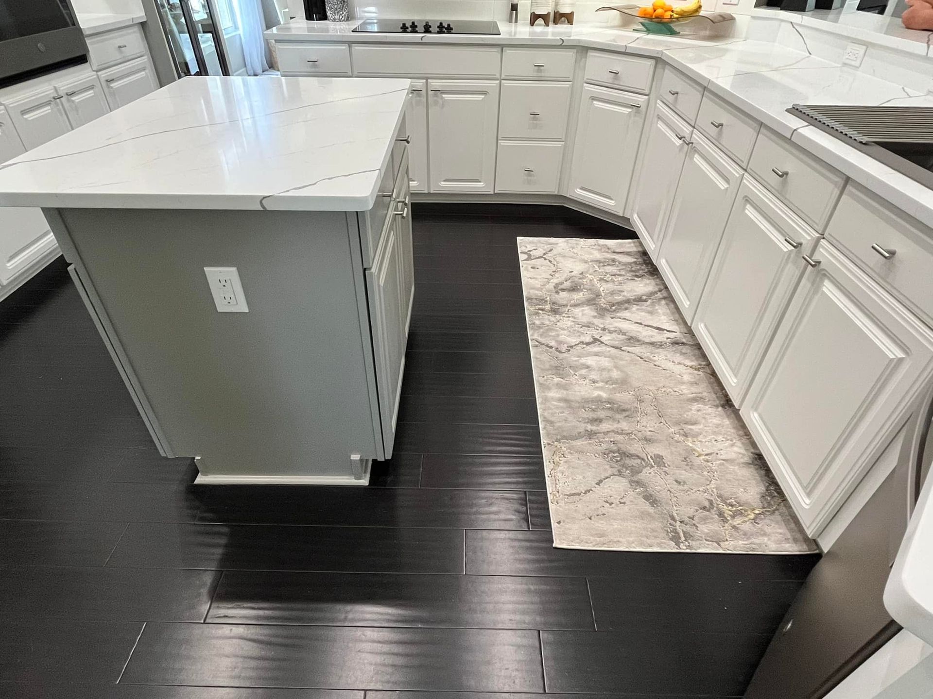 Kitchen with white cabinets, gray island, dark wood floor, and a patterned rug.