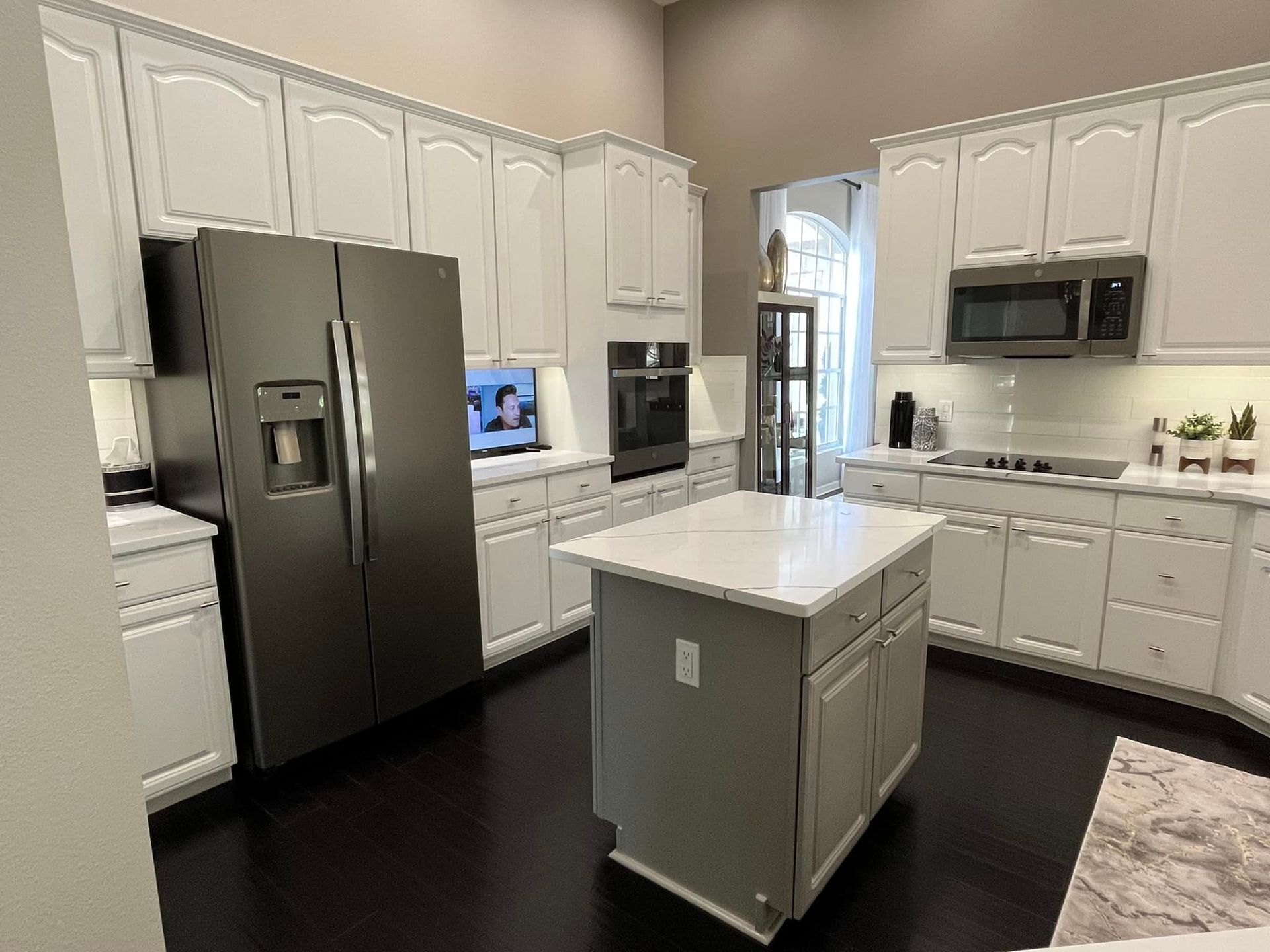 Modern kitchen with white cabinets, stainless steel appliances, dark wood floors, and a gray island.
