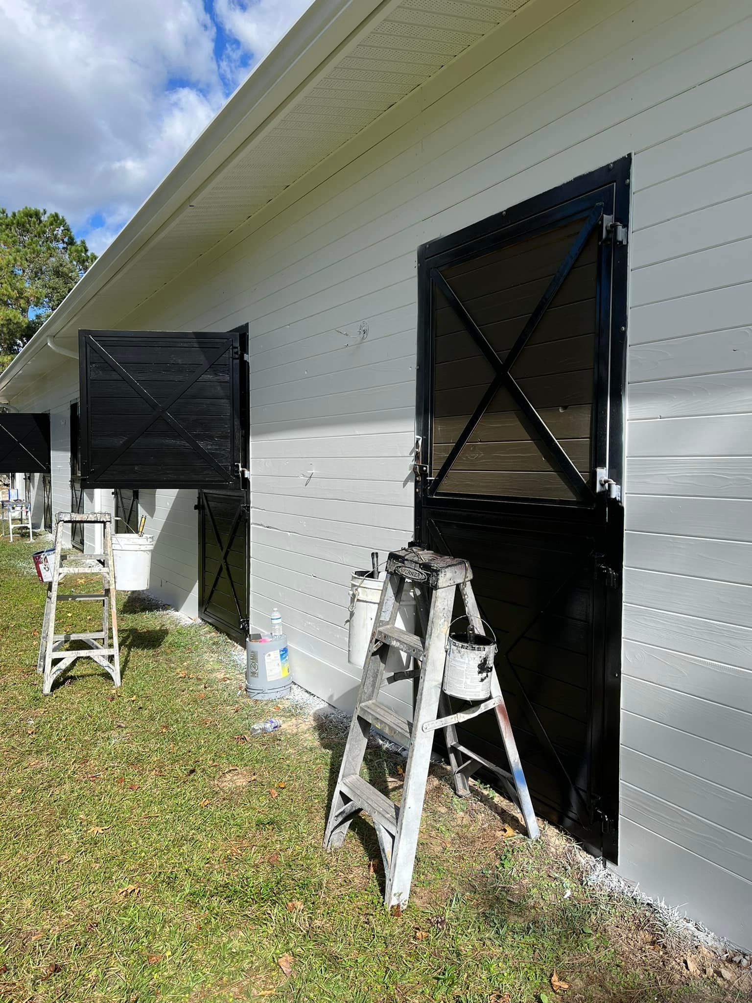 White barn with black doors and shutters, painting supplies nearby.
