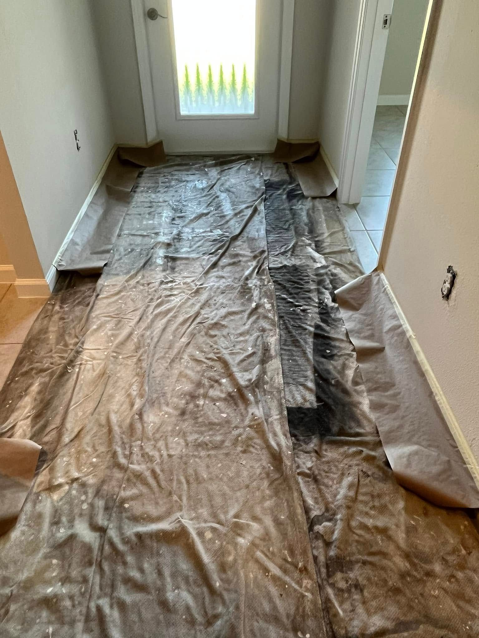 Hallway with brown paper and plastic covering the floor, leading to a door with a window.