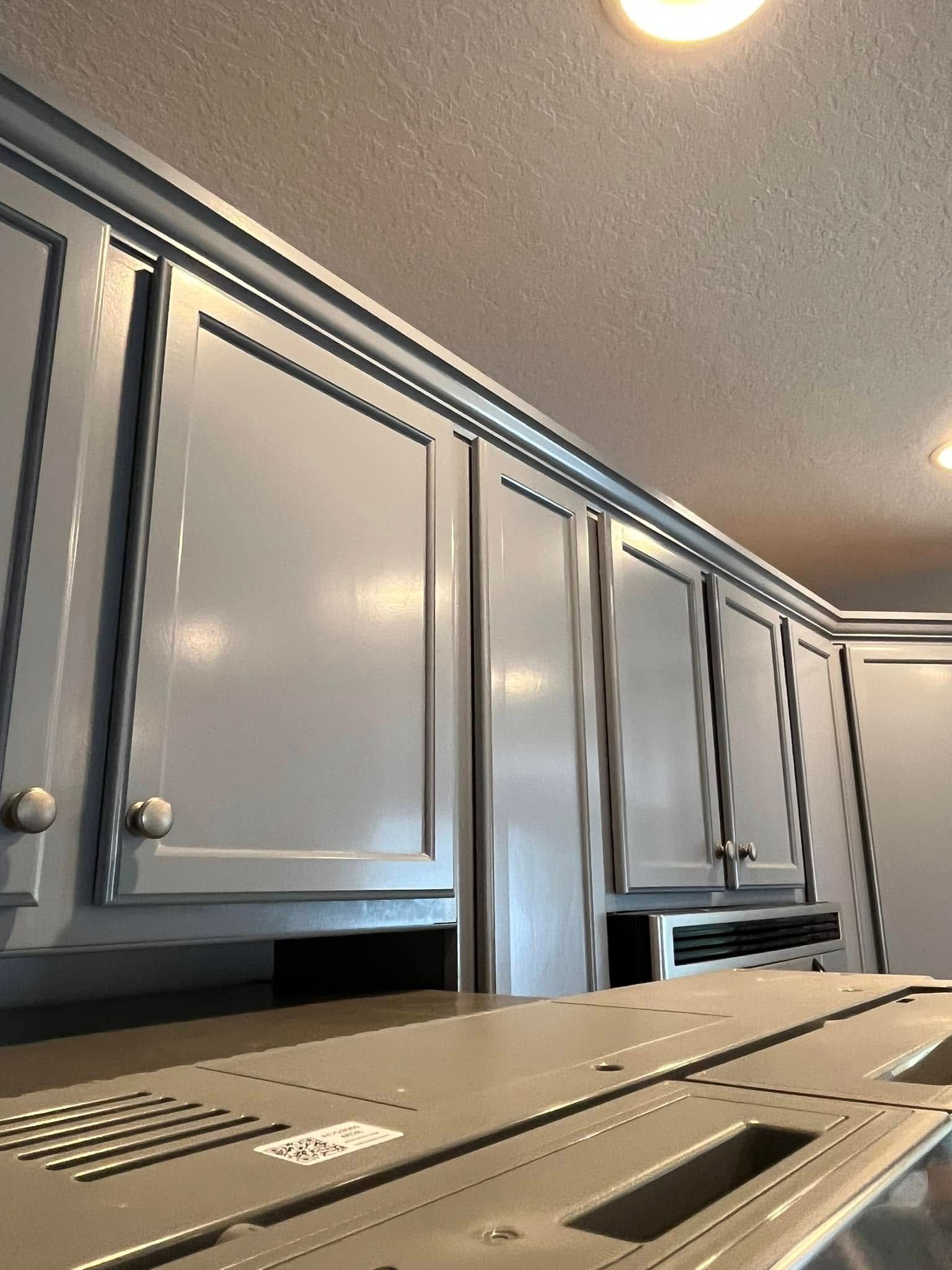 Gray kitchen cabinets with silver trim against a white ceiling, angled view.