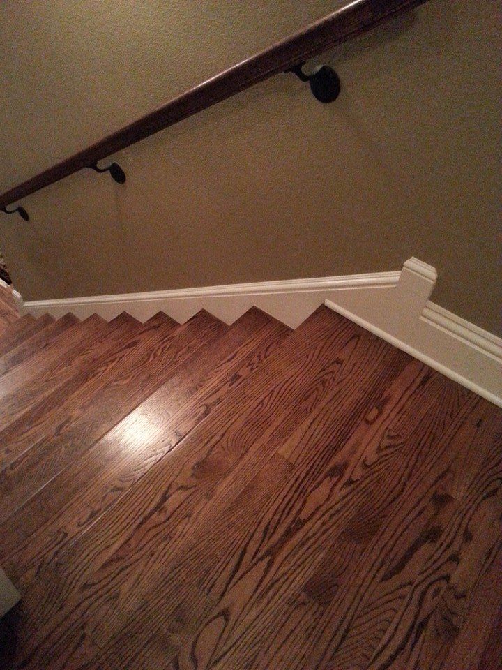 Wooden staircase with a dark handrail against a beige wall, viewed from above.