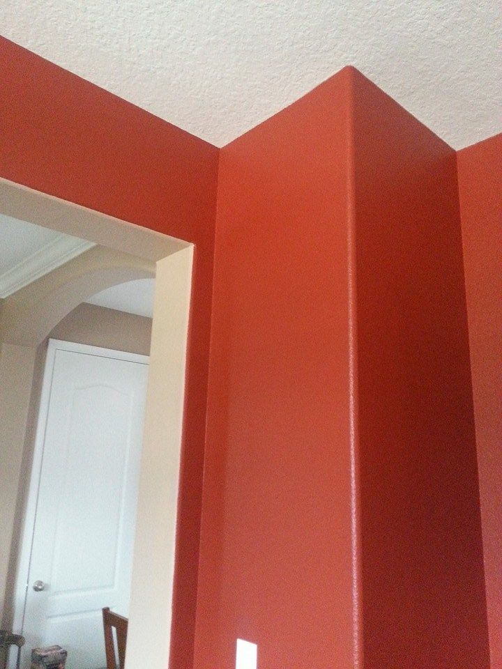 Corner of red painted walls meeting a white ceiling. A doorway with beige trim is visible.