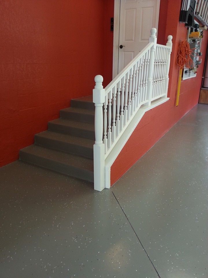 Gray stairs with white railing against a red wall, leading to a white door in a garage.