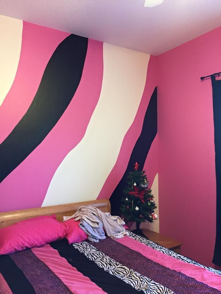 Pink, black, and white zebra-striped wall in bedroom, Christmas tree, bed with pink bedding and pillows.