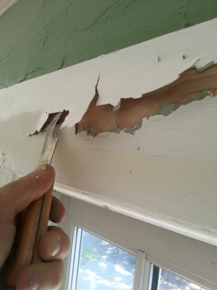 Hand using a chisel to remove peeling white paint from a windowsill.