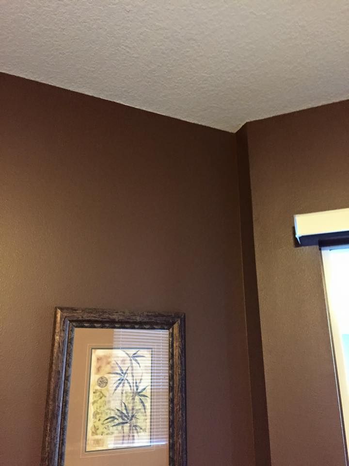 Brown walls with a white textured ceiling, framed artwork, and a window partially visible.