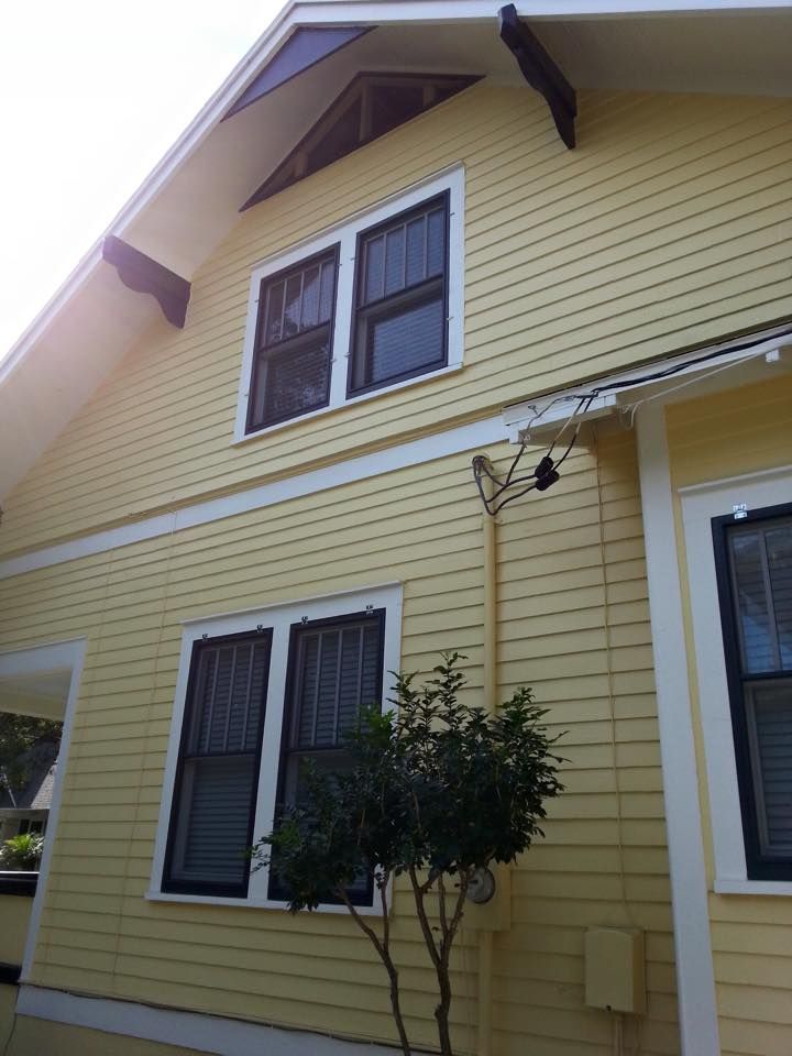 Yellow house with dark-framed windows, white trim, and a small tree.