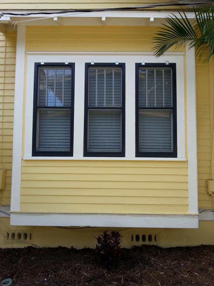 Three windows with black frames and white trim on yellow clapboard siding.