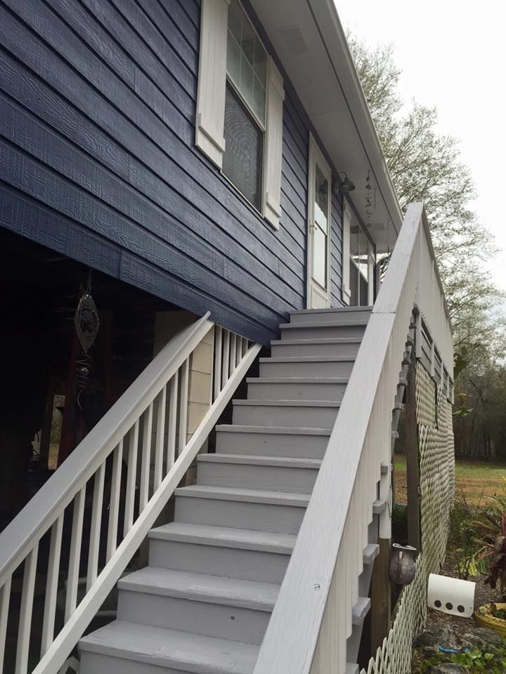 Exterior view of a house with a staircase leading to the front door, blue siding, and white railings.