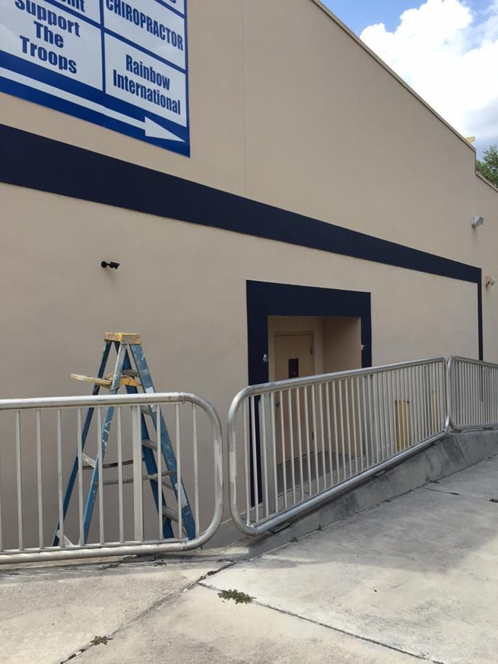 Exterior view of a building with a ramp and metal railing. A blue ladder stands next to the building's entrance.