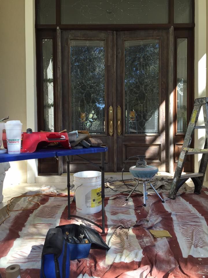 Exterior view of a home's entryway with work supplies on a covered porch, including tools and a ladder.