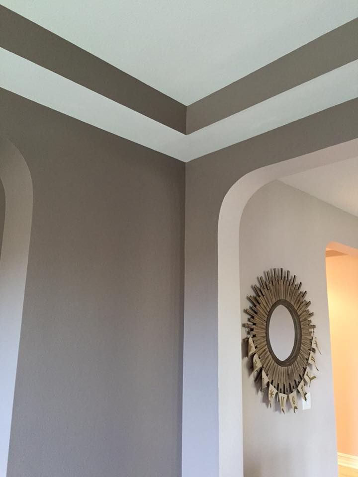 Corner of a room with taupe walls and white trim. A sunburst mirror hangs on an adjacent wall.
