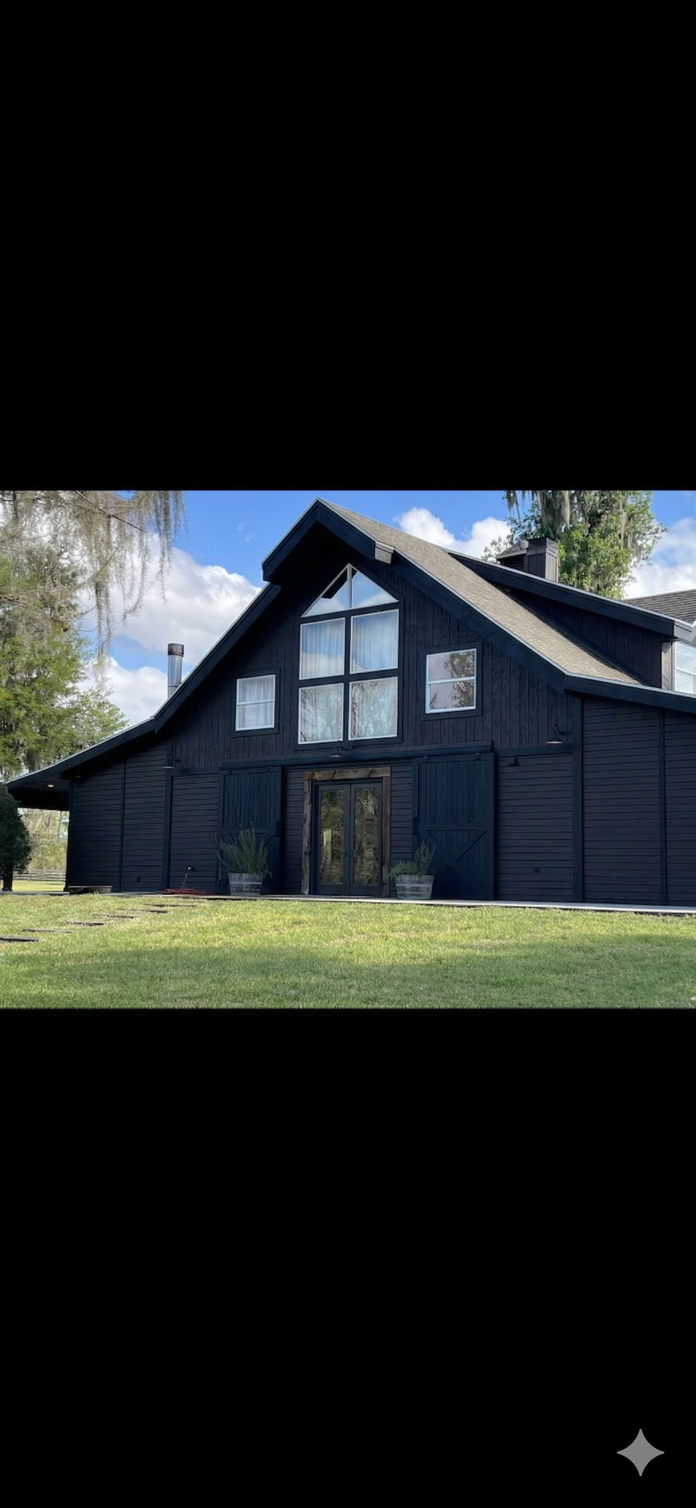Black barn-shaped house with large windows under a blue sky. Green grass in front.
