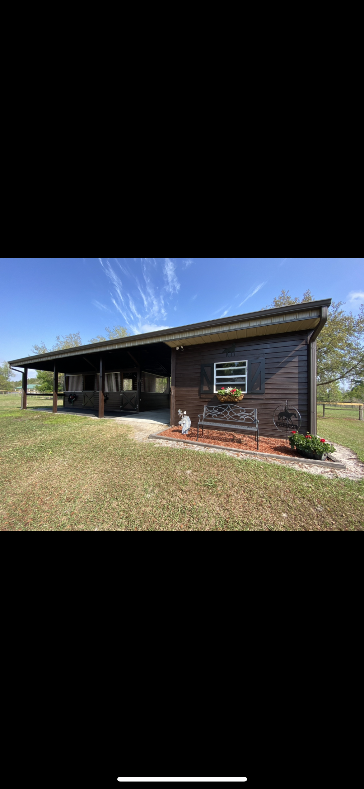 A dark brown cabin with a long porch sits in a grassy field under a blue sky.