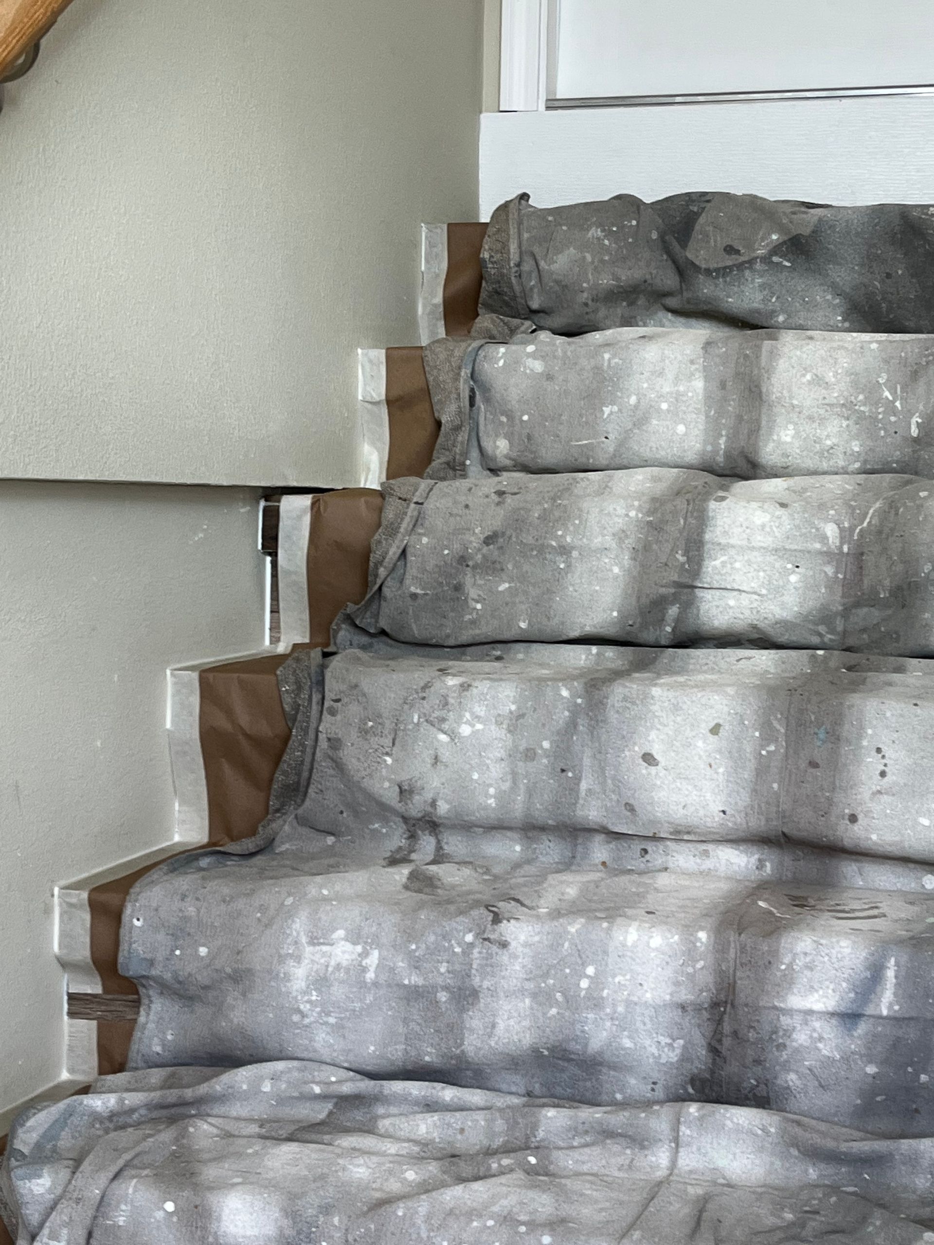 Stone steps covered in grey protective material. Brown paper taped to sides near a wall.