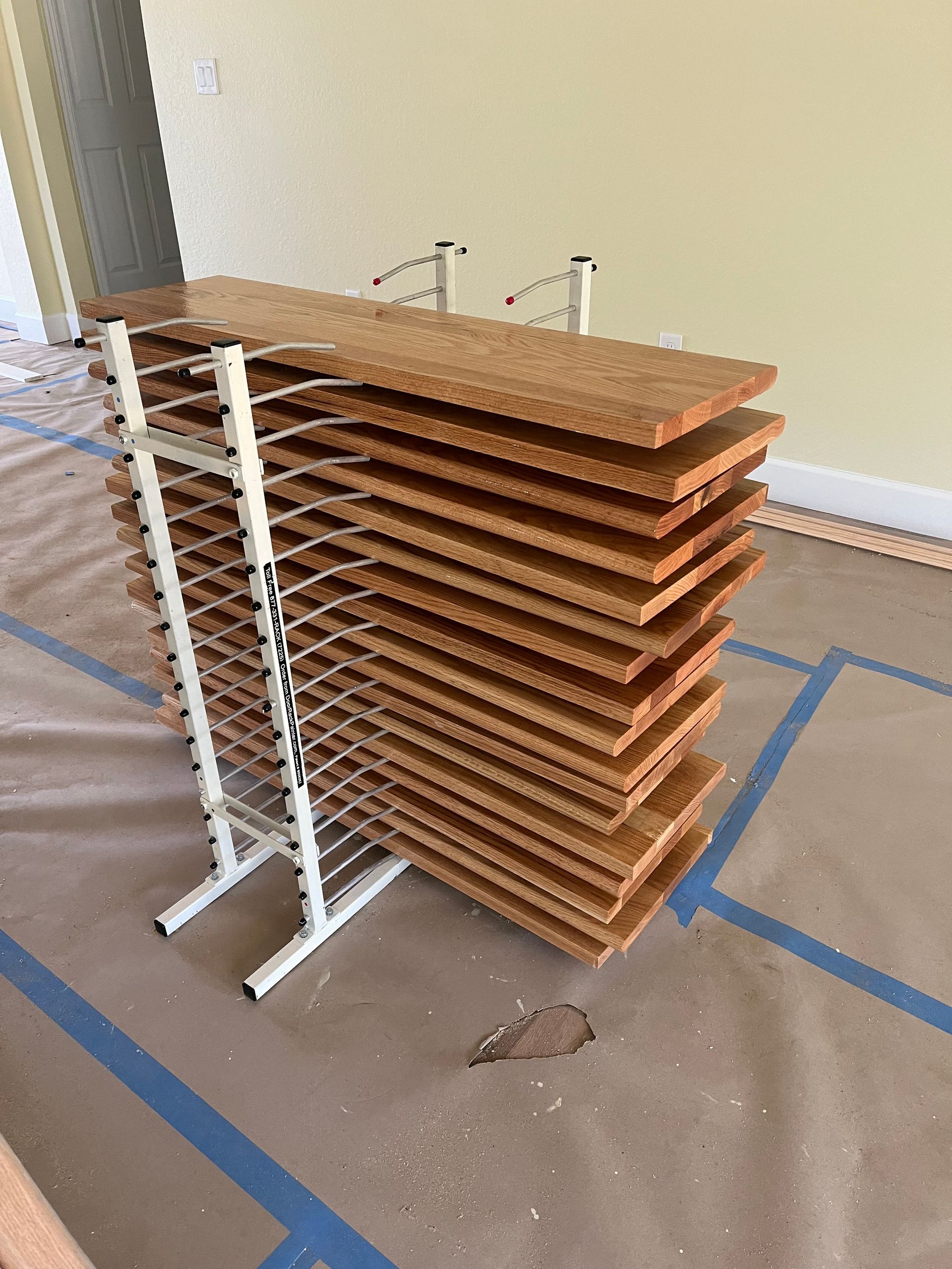 Wooden planks stacked on a white drying rack, set on a drop cloth.