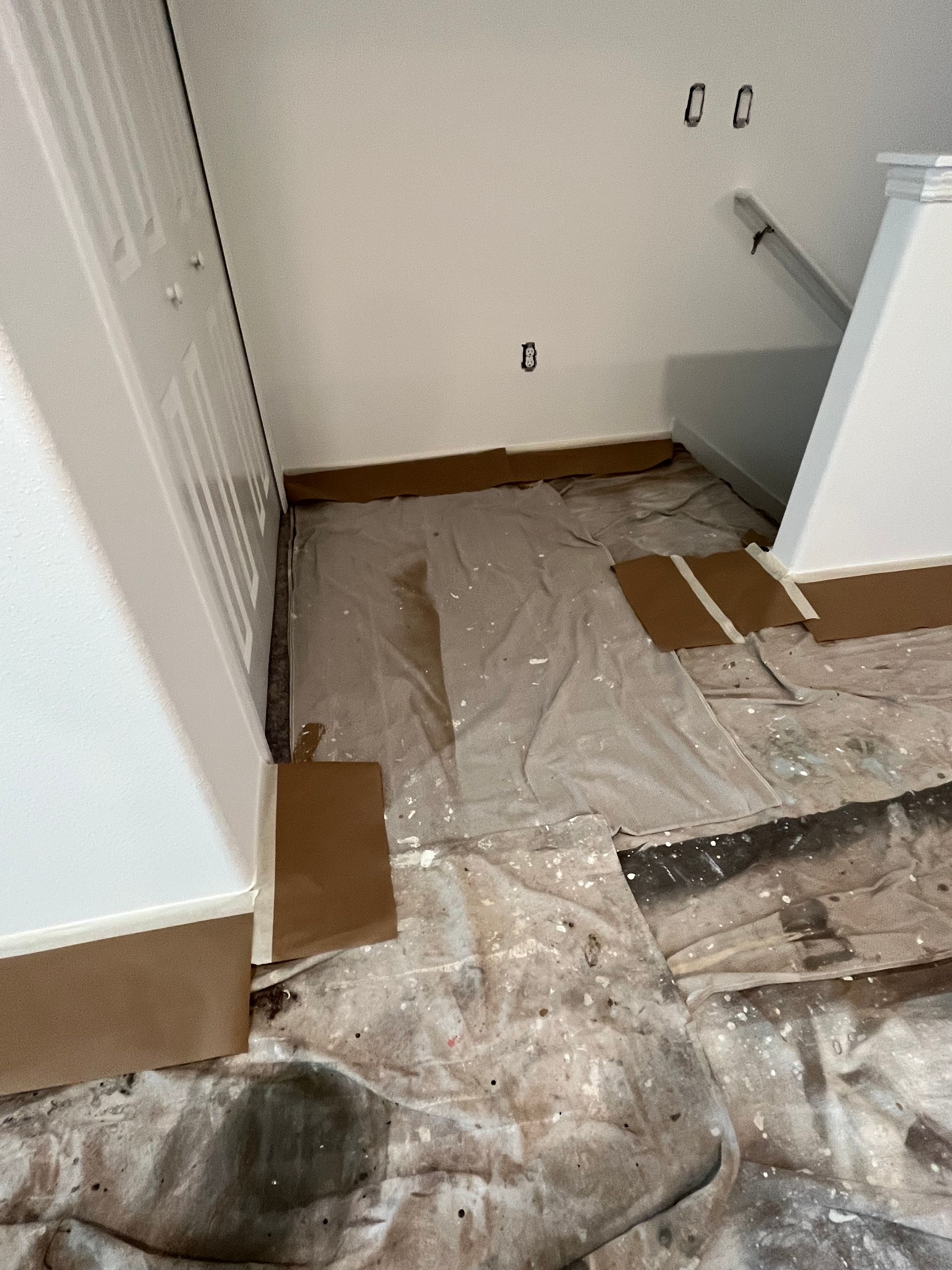 A room with a partially covered floor in preparation for renovations. White walls, brown trim.