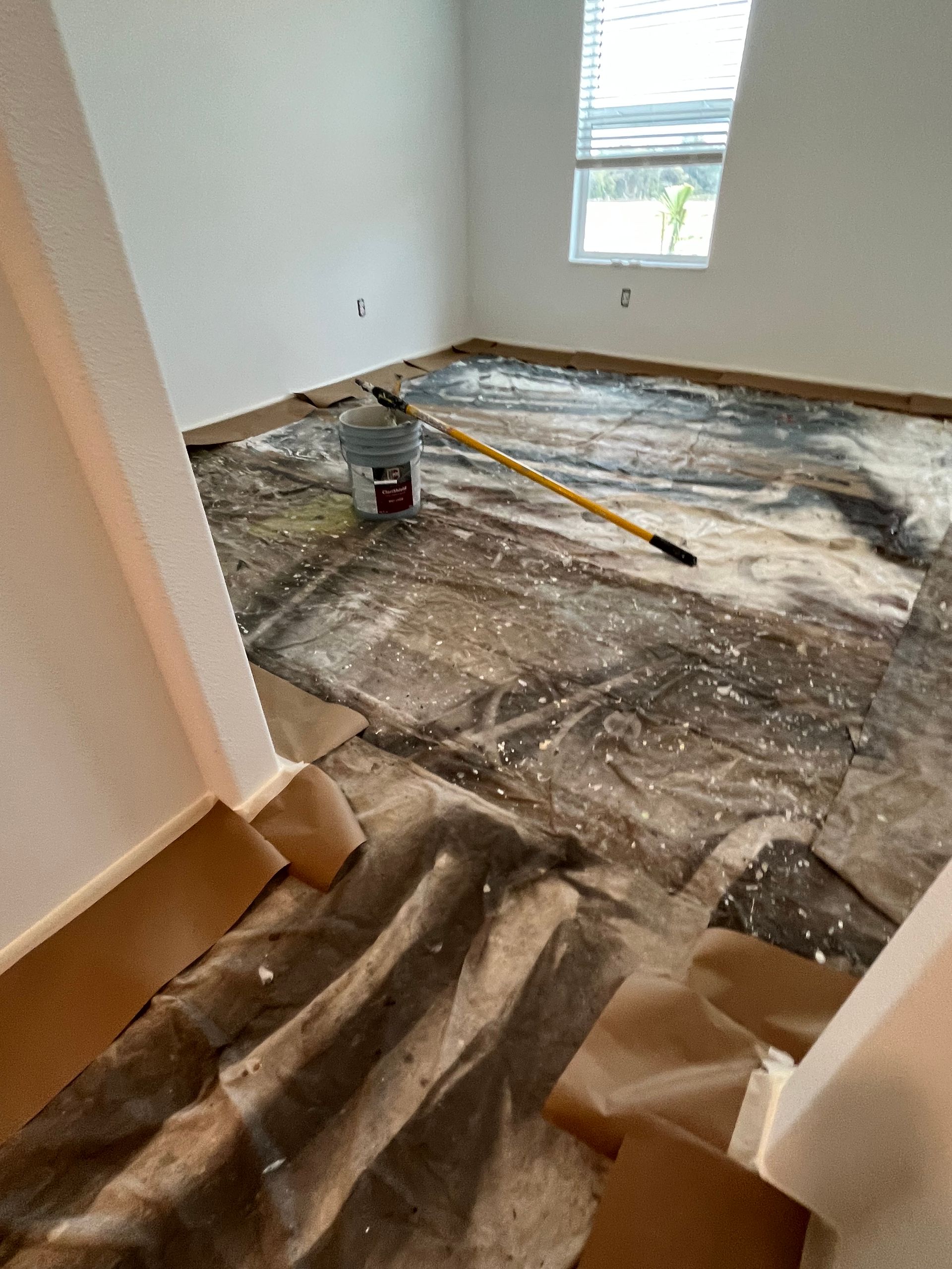Room with flooring being removed; debris and paint bucket visible. Light coming from a window.
