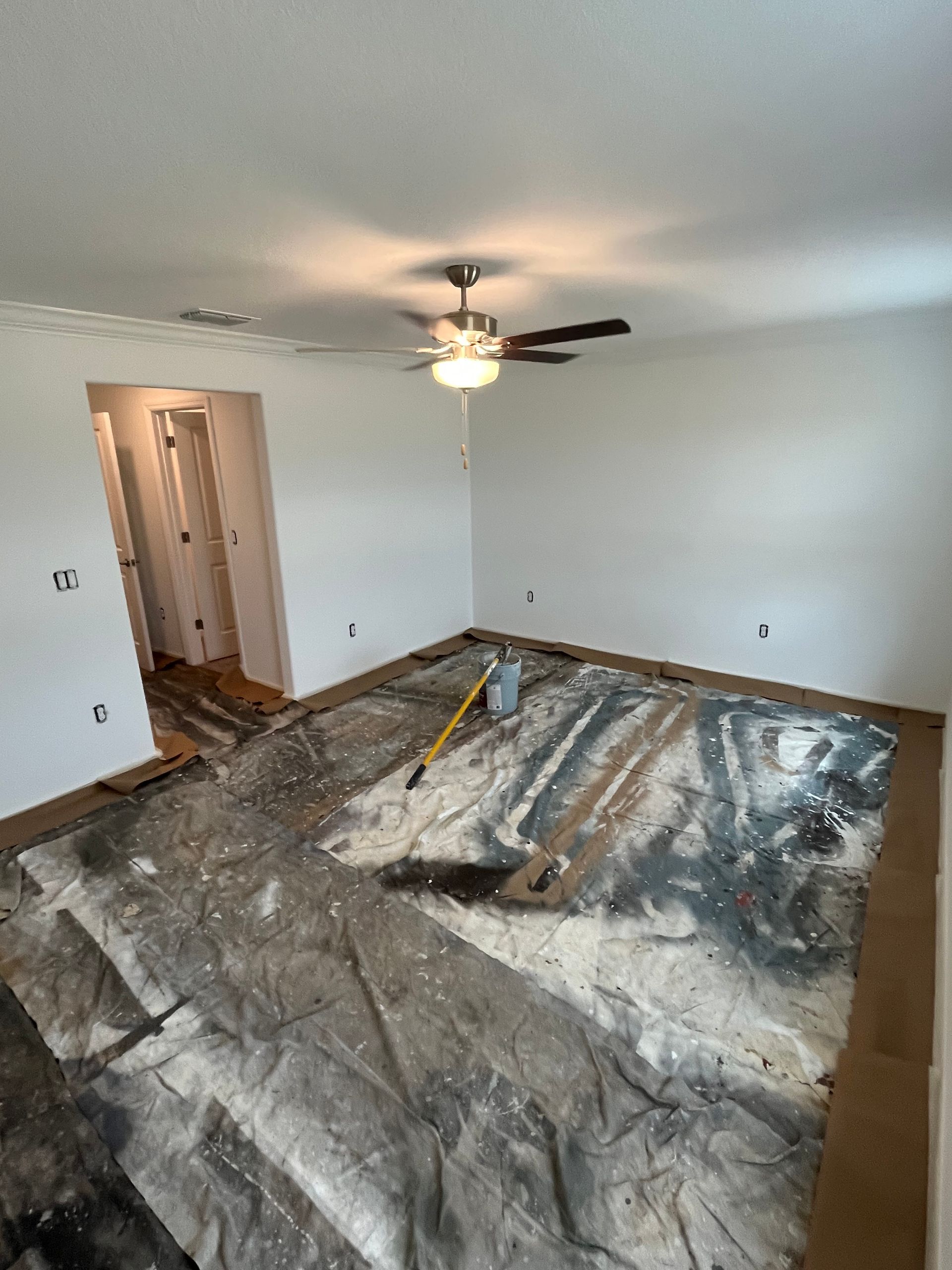 Room under renovation; protective sheeting covers floor; debris scattered; walls painted white.