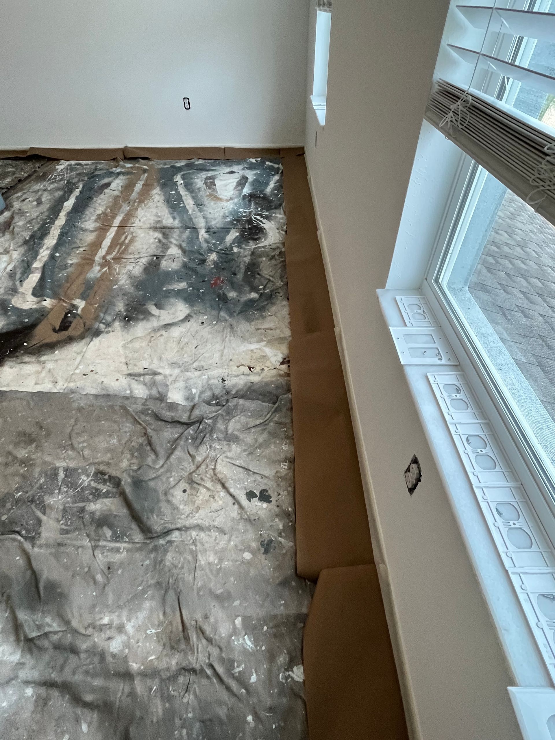 Room with tarp-covered floor, wall with window, and a section of exposed floor.