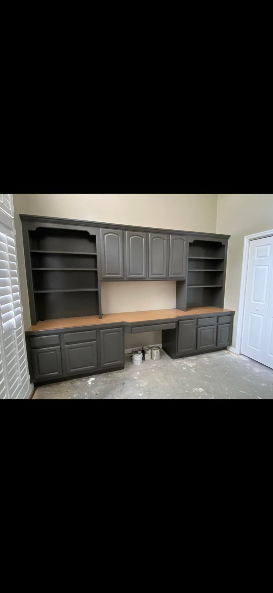 Built-in desk with dark gray cabinets, open shelving, and a light-colored countertop. Located in a room.