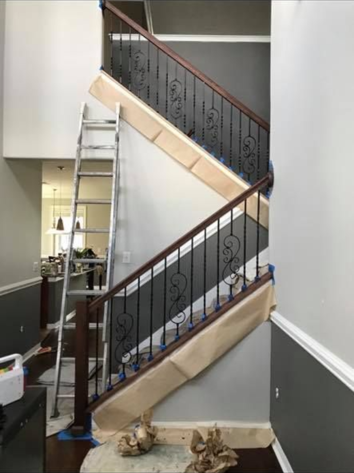 Staircase with dark wooden handrails, black iron balusters, and a ladder leaning against the wall during renovation.