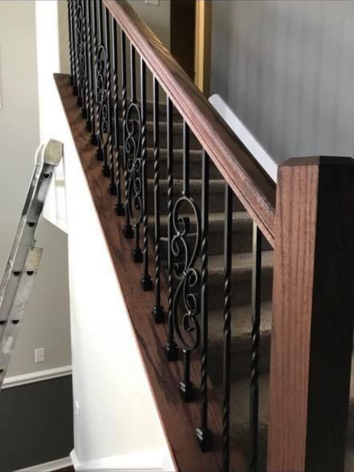 Staircase with wooden handrails and decorative black iron spindles, leading upwards.