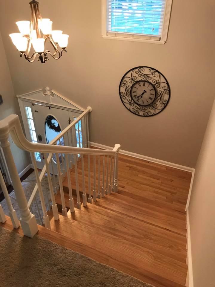 Wooden staircase with white railing, leading down to a front door with a chandelier and clock above.