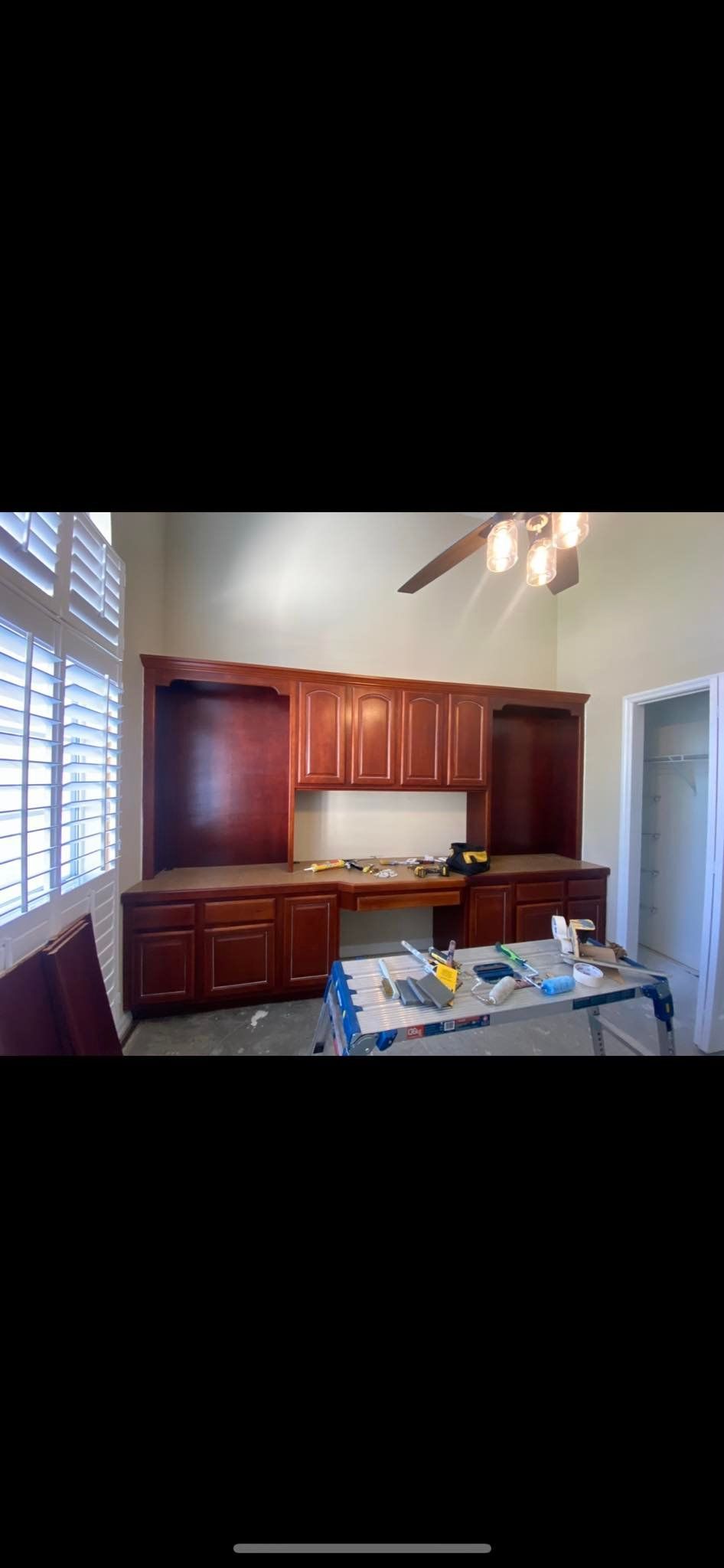 Dark brown built-in desk with cabinets and storage in a room with a window and a ceiling fan.