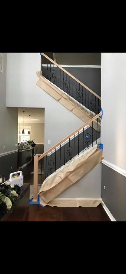 Interior staircase with dark wood floor, gray walls, and black railing with protective paper covering.