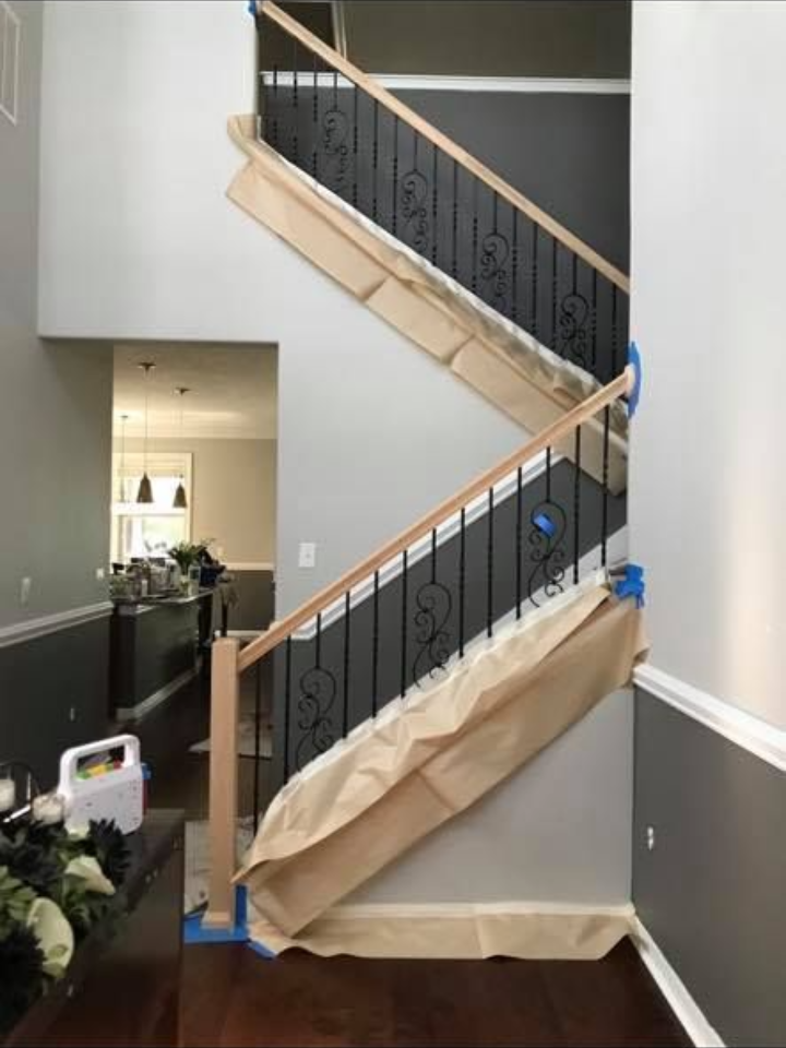 Staircase with black wrought iron railings, light wood handrails, and gray walls, protected by paper during renovations.