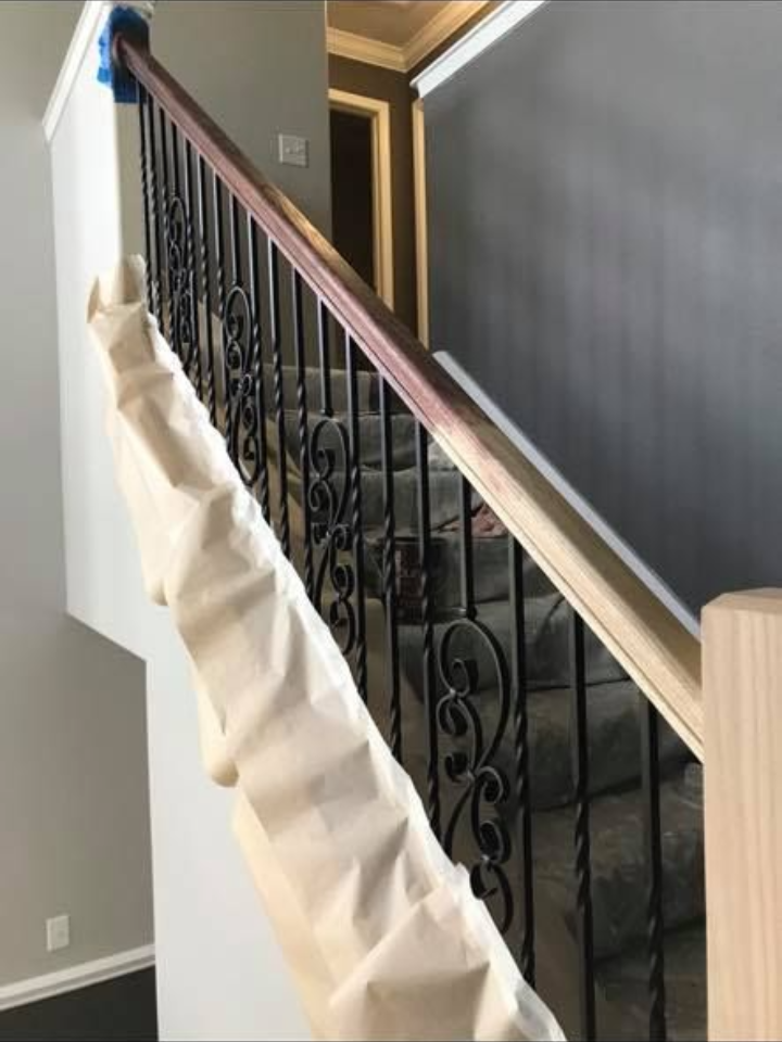 Staircase with wooden handrail, ornate black iron balusters, and gray carpeted steps.
