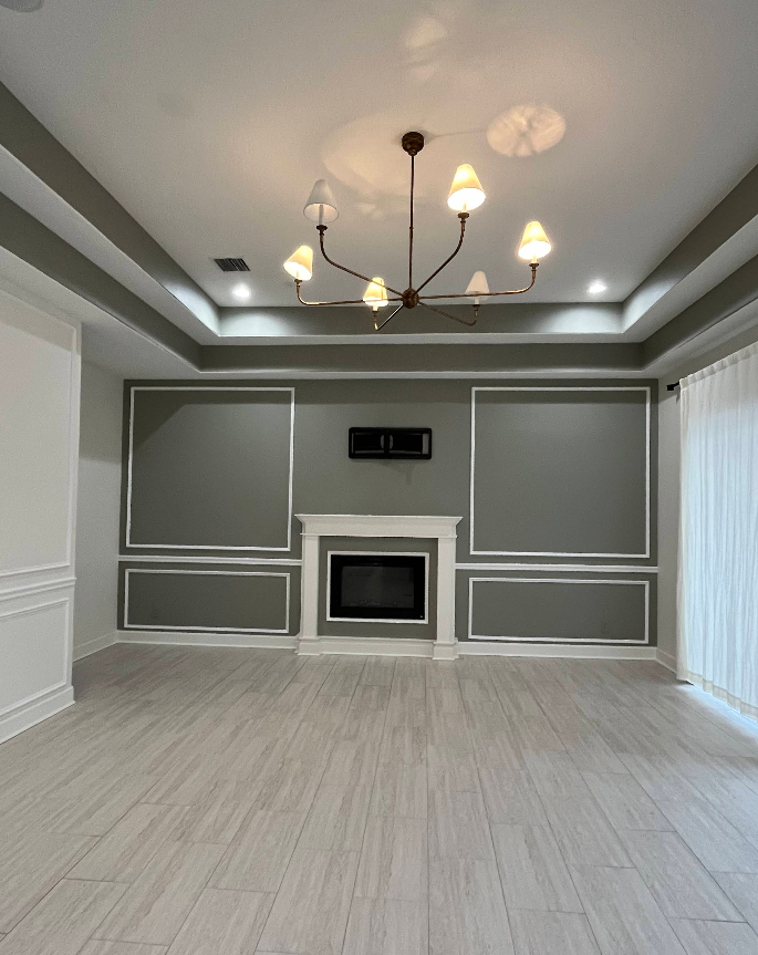 Empty living room with fireplace, gray paneling, and a chandelier. Light wood flooring.