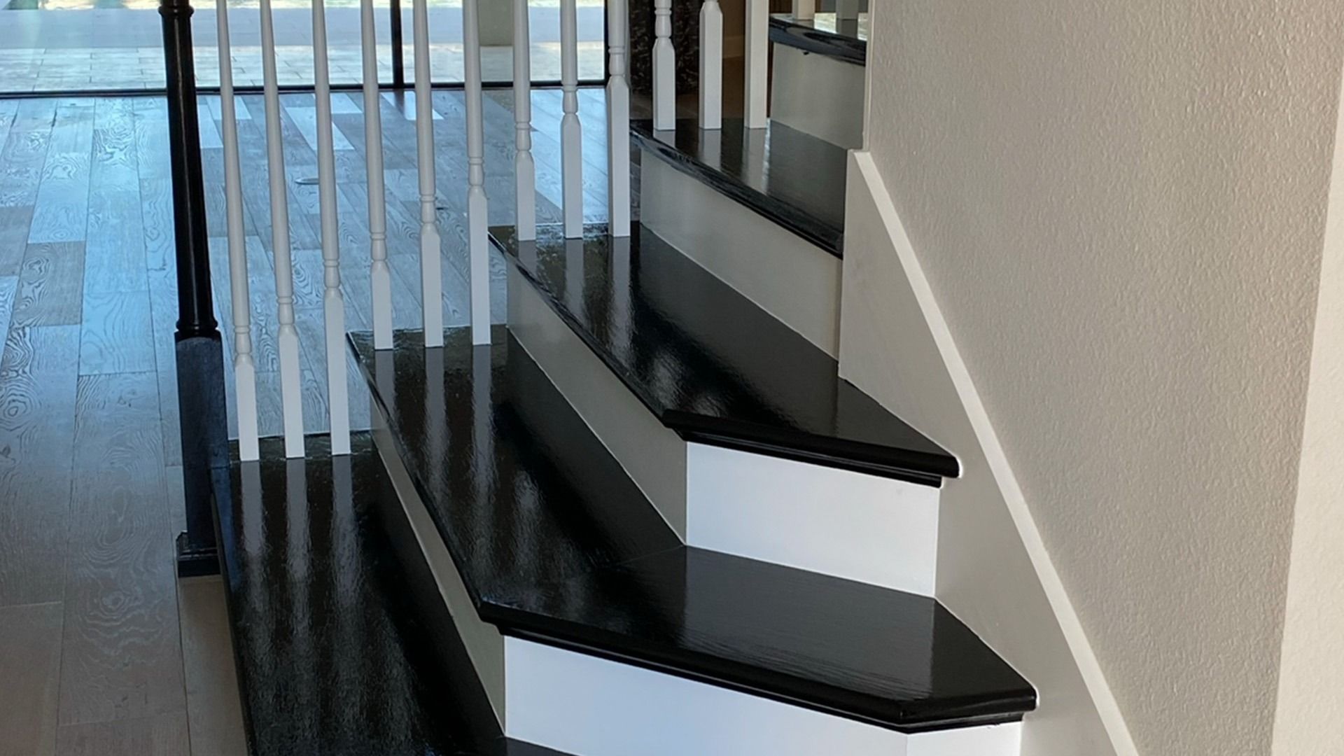 Black and white staircase with wooden handrail, white risers, and glossy black treads.