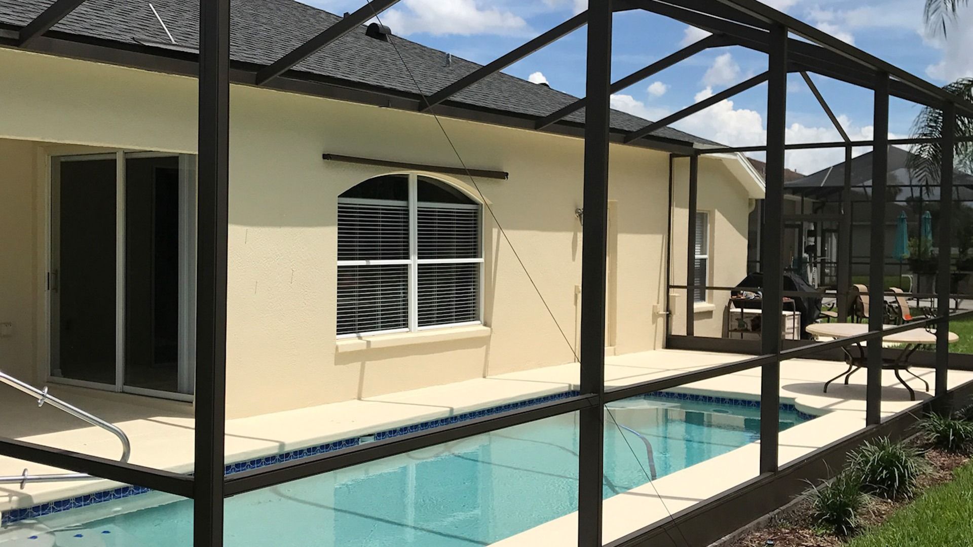 Beige house with a screened pool enclosure; small pool, blue water, sunny day.