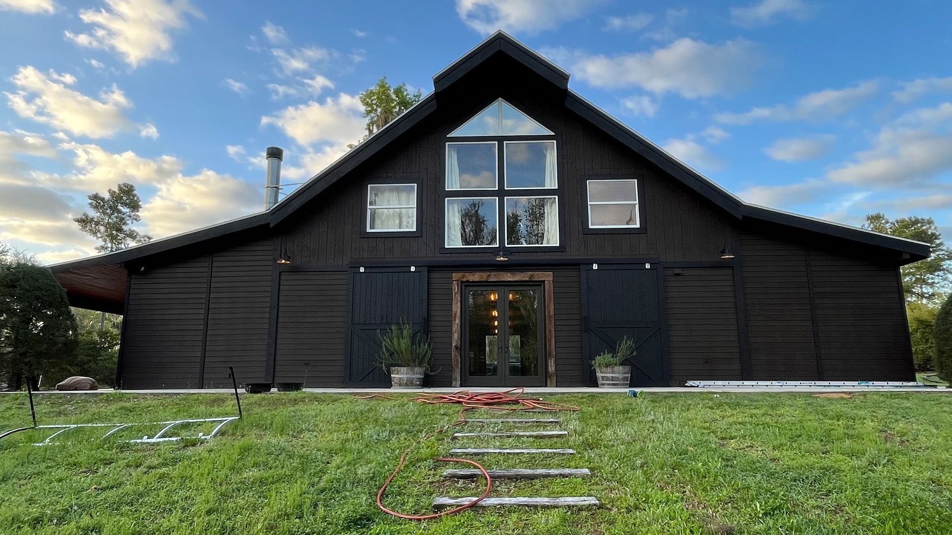 Black barn house with large windows, sliding doors, and a small front yard with steps.