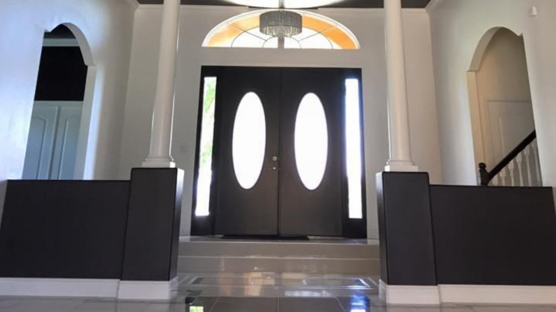 Double front doors with oval windows, flanked by pillars and side lights, leading into a home.