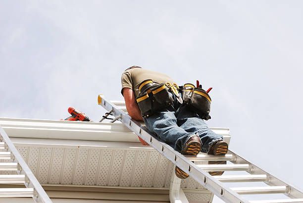 A man is sitting on a ladder working on the roof of a house.