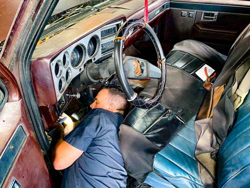 A man is laying under the dashboard of a car.