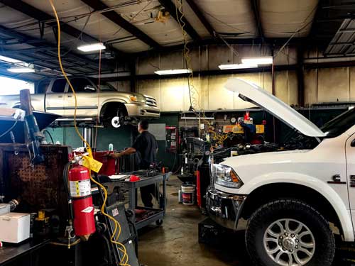 A man is working on a truck in a garage with the hood open.